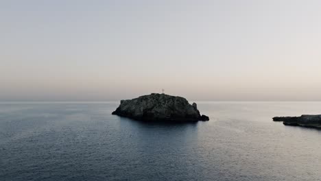 Aerial-footage-in-the-sunrise-pulling-away-from-the-small-island-of-Scoglio-dell'Eremita-in-southern-Italy