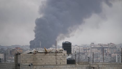 Thick-black-smoke-rises-high-among-buildings-destroyed-by-Israeli-missile-attacks-in-the-Gaza-Strip,-Palestine