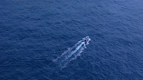 Drone-tilt-up-as-small-fishing-boat-cross-deep-blue-shimmering-ocean