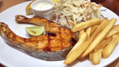 A-plateful-of-flavourful-food-served-in-a-restaurant,-a-combinaion-of-grilled-salmon-steak,-french-fries,-and-coleslaw-salad