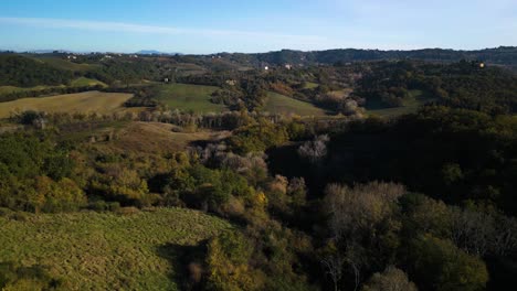 Drone-descends-into-ravine-of-Tuscan-forested-orchard-landscape-in-autumn