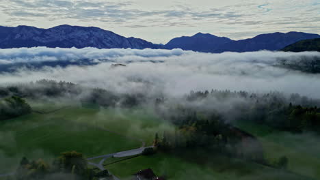 A-Reverse-Aerial-Shot-Of-A-Small-Village-At-A-Rustic-Landscape-Covered-In-Mist-In-Austria