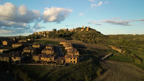 Golden-hour-glow-on-Val-d'Orcia-Tuscany-village-with-orchards-and-farm-fields,-aerial-panoramic