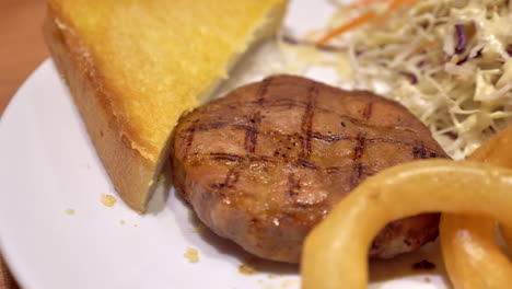 A-serving-of-beef-burger-steak-and-side-dishes-of-butted-toast,-onion-rings,-and-coleslaw-salad,-served-in-a-restaurant-in-Bankok,-Thailand