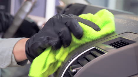 Engineer-wearing-black-gloves-and-using-green-microfiber-cloth-to-clean-up-car-dashboard