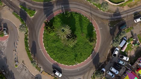 Drone-rises-above-roundabout-in-Caribbean,-rotating-as-cars-exit-the-road