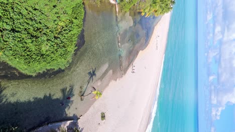 Vertical-flight-over-sandy-beach-of-Los-Patos-with-tourist-and-river-during-sunny-day---Caribbean-Blue-Sea-in-Background