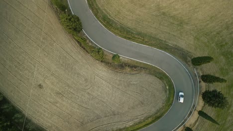 Aerial-top-down-bird's-eye-view-of-SUV-driving-along-winding-road-in-Tuscany-Italy