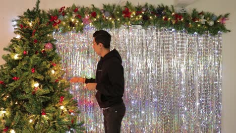Young-mexican-man-decorating-christmas-tree-in-festive-room,-timelapse