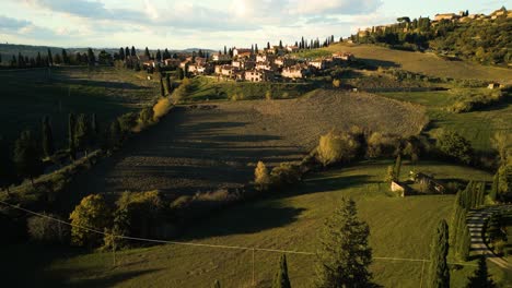 Golden-hour-light-glows-across-rolling-hills-landscape-of-Val-d'Orcia-Tuscany-with-quaint-village