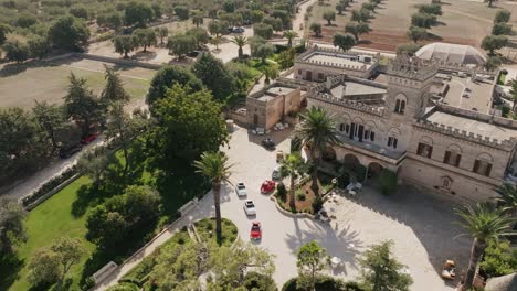 Aerial-footage-rotating-around-the-front-parking-lot-of-a-masseria-in-southern-italy-with-a-lot-of-small-colorful-cars-parked-there