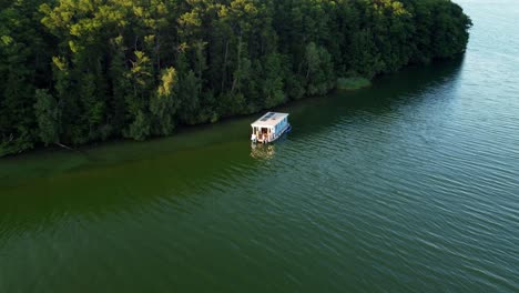House-boat-floating-on-a-lake-next-to-a-huge-island-covered-in-trees-in-Brandenburg,-Germany