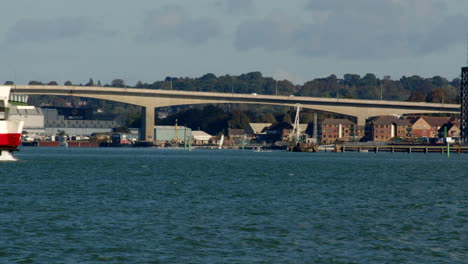 Die-Rote-Trichterfähre-Der-Isle-Of-Wight-Betritt-Das-Bild-Am-Solent-Southampton-Mit-Einem-Segelboot-Und-Einer-Itchen-Mautbrücke-Im-Hintergrund