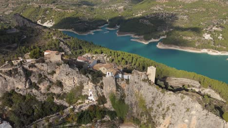 Reverse-drone-view-of-the-castle-of-Guadalest-and-the-blue-lake,-revealing-the-landscape