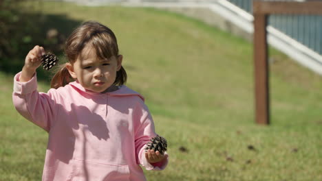Cute-Little-Girl-Caring-Pine-Strobiles-or-Cones-in-Both-Hand-and-Walking-Though-Grass-Lawn-in-Slow-Motion