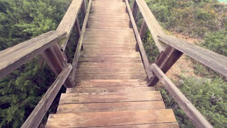 Walking-down-the-wooden-promenade-stairways-pathway,-revealing-sea-water-surface,-daytime-outdoor-capture,-recreation,-and-free-time-activities-concept