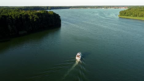 Small-yacht-driving-on-a-lake-surrounded-by-a-forest-in-Brandenburg,-Germany
