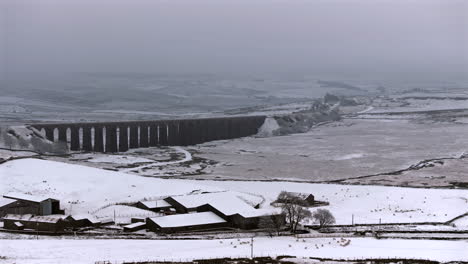 Erstellung-Einer-Luftdrohnenaufnahme-Des-Verschneiten-Ribblehead-Viadukts-Und-Der-Farm-In-Yorkshire-Dales,-Großbritannien