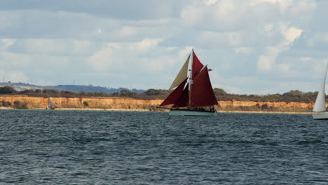 shot-of-red-jet-powered-catamaran-ferry-entering-frame-in-front-of-Gaff-Cutter-called-Golden-Vanity-and-a-sailboat-on-the-Calshot-spit-by-the-Solent,-Southampton