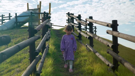 Sad-little-girl-walking-down-the-hill-trail-with-wooden-fence-at-countryside-playground