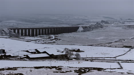 Establishing-Aerial-Drone-Shot-of-Ribblehead-Viaduct-and-Farm-on-Snowy-Day-in-Yorkshire-Dales-UK