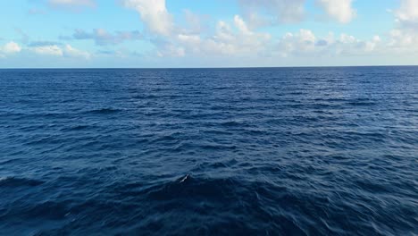 Low-aerial-dolly-flies-parallel-over-deep-blue-Caribbean-water-with-fluffy-clouds-in-distance