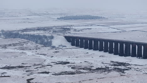 Establishing-Aerial-Drone-Shot-of-Ribblehead-Viaduct-on-Snowy-Misty-Dark-Day-in-Yorkshire-Dales-UK