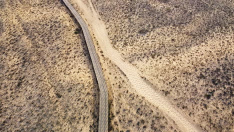 Aerial-tilt-up-shot-of-sandy-dunes-path-and-blue-Atlantic-ocean-during-golden-sunset-in-Portugal