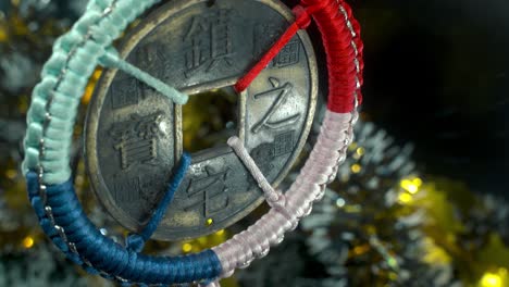 Dreamy-close-up-shot-of-a-Chinese-ancient-traditional-lucky-coin,-Asian-New-Year-decoration,-shiny-blur-Christmas-background,-square-hole-colorful-strings,-culture-holyday-symbol,-smooth-tilt-up-4K