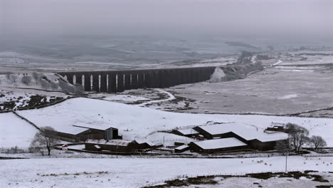 Establishing-Aerial-Drone-Shot-of-Snowy-Ribblehead-Viaduct-in-Yorkshire-Dales-and-Farm-in-Foreground-UK