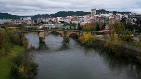 Aerial-pan-around-Ourense-Roman-Bridge-on-Miño-River-in-Ourense,-Galicia,-Spain-in-autumn