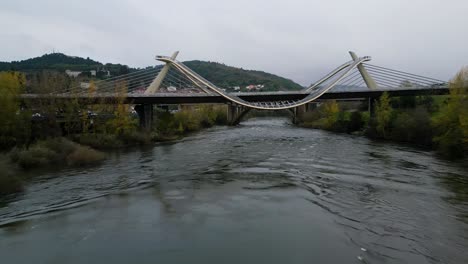 Millennium-Bridge-over-the-Miño-River-in-Ourense,-Galicia,-Spain,-drone-dolly-below-winding-path