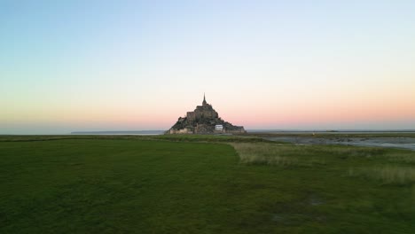 Aerial-Drone-View-of-Mont-Saint-Michel-Flying-Over-Grass-from-Left-to-Right-at-Sunset