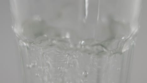 Slowmotion-macro-of-still-water-pouring-into-clear-glass-in-front-of-neutral-background