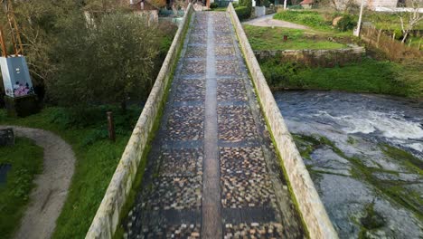 Plataforma-Rodante-Sobre-Un-Puente-De-Piedra-Cubierto-De-Musgo-Que-Cruza-El-Río-Lonia-En-Ourense,-España
