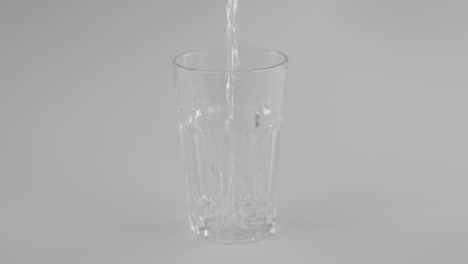 Locked-slowmotion-still-water-pouring-into-clear-glass-in-front-of-neutral-background