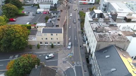 Drone-shot-moving-up-from-overhead-bustling-city-street-to-sunset-skyline-over-Galway,-Ireland