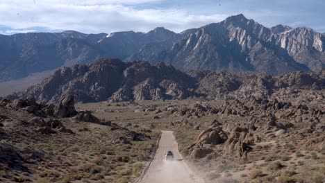 White-off-road-SUV-driving-away-on-a-dirt-road,-towards-the-Eastern-Sierra-mountains,-in-the-desert