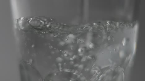 Slowmotion-Makro-Von-Stillem-Wasser,-Das-Vor-Dunklem-Hintergrund-In-Klares-Glas-Fließt