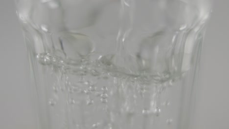 Slowmotion-Makro-Von-Stillem-Wasser,-Das-Vor-Neutralem-Hintergrund-In-Klares-Glas-Fließt