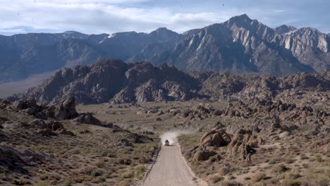 White-off-road-SUV-driving-to-the-camera-on-a-dirt-road,-away-from-the-Eastern-Sierra-mountains,-in-the-desert