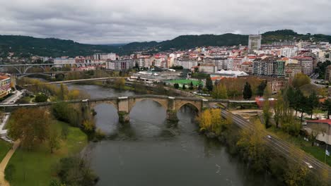 Drone-ascends-to-reveal-Ourense-Roman-Bridge-on-Miño-River-in-Ourense,-Galicia,-Spain