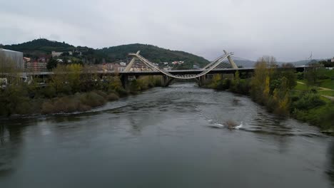 Slow-aerial-dolly-above-river-to-Millennium-Bridge-Miño-River-in-Ourense,-Galicia,-Spain-as-seagull-soars