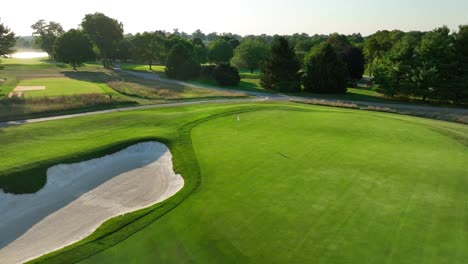 Golf-course-during-summer-sunset-Aerial-view-of-sand-bunker-and-well-maintained-green-with-flag-at-hole