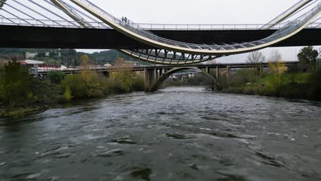 Drone-flies-below-Millennium-Bridge-Miño-River-in-Ourense,-Galicia,-Spain-pulling-back