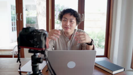 Asian-man-sitting-on-with-laptop-and-talking-to-camera