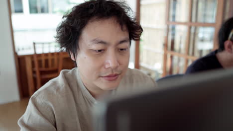 Lächelnder-Asiatischer-Mann,-Der-Im-Café-Am-Laptop-Arbeitet