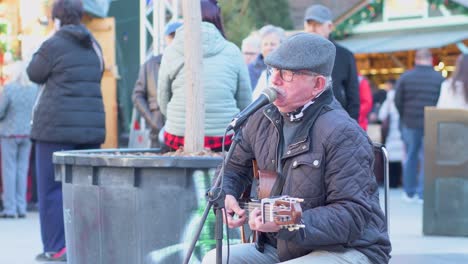 Senior-man-in-cap-singing-and-playing-guitar-on-the-street-on-a-frosty-day