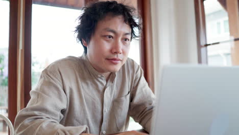 Hombre-Asiático-Mirando-Una-Computadora-Portátil-Plateada-En-La-Cafetería-Durante-El-Día