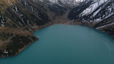 Aerial-shot-tilting-over-the-Big-Almaty-Lake,-revealing-snowy-mountains-of-Kazakhstan